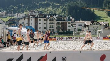 Group games on the beach with several children. In the background, mountains and modern buildings can be seen.