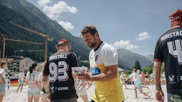 A group of people in sportswear on a sandy beach. In the background, mountains and a blue sky can be seen.