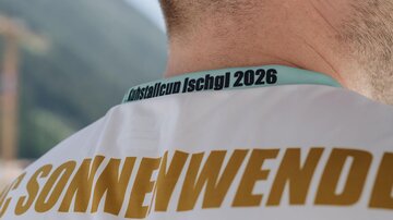 A man is wearing a T-shirt with the name "Sonnenwende" and a print for the "KristallCup Ischgl 2026". The atmosphere feels sporty and enthusiastic.