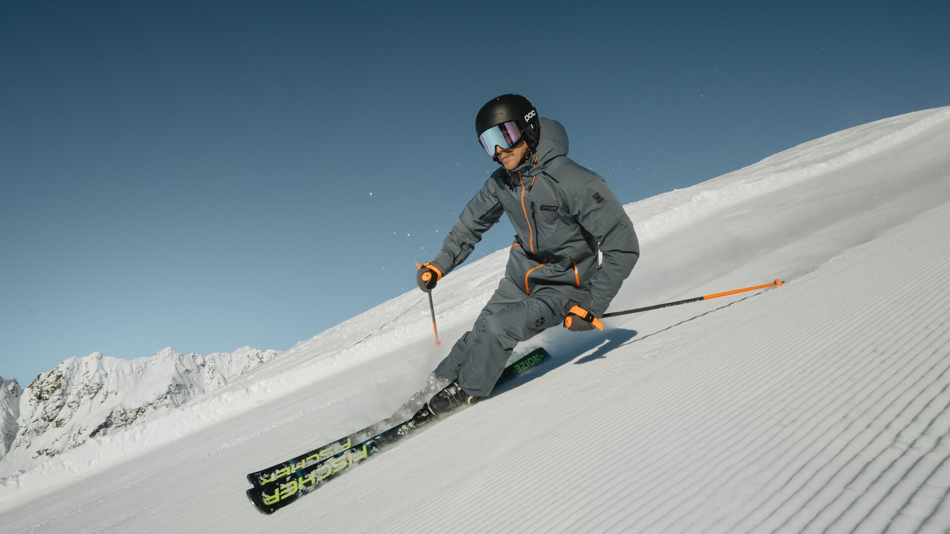 Ein Skifahrer fährt über die frisch präparierte Piste. Der Himmel ist klar und die Berge sind im Hintergrund sichtbar.
