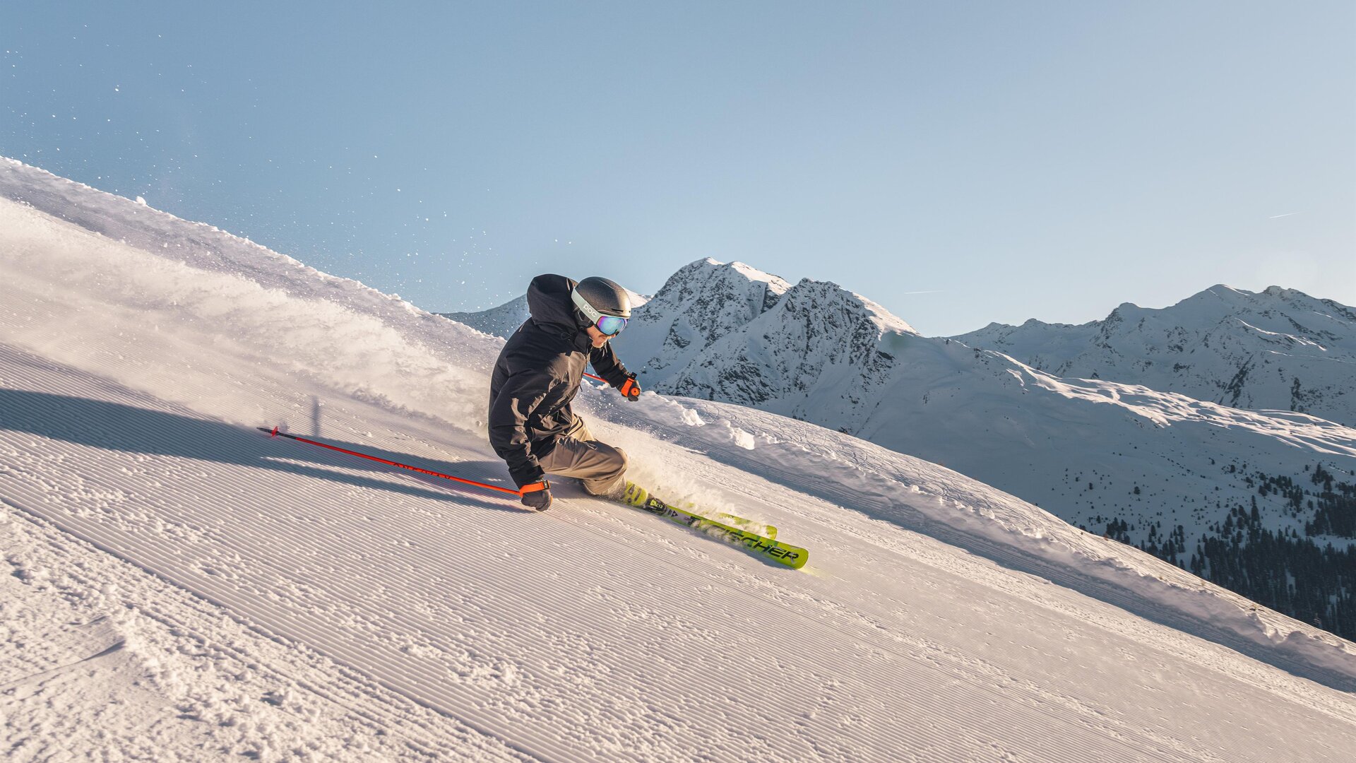Ein Skifahrer fährt die schneebedeckte Piste hinunter. Im Hintergrund sind majestätische Berge zu sehen.