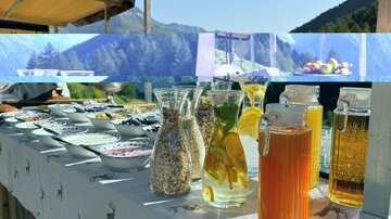 A beautifully decorated table outdoors with various drinks and snacks. In the background, green mountains and a clear sky are visible.