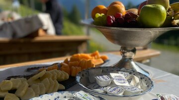 A set table with various snacks, including fruit and cheese. In the background, mountains and a beautiful landscape are visible.
