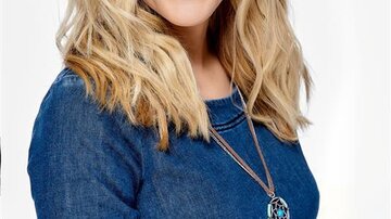 A laughing woman with long, curly blonde hair is wearing a denim top. She is looking directly at the camera and radiates a friendly atmosphere.