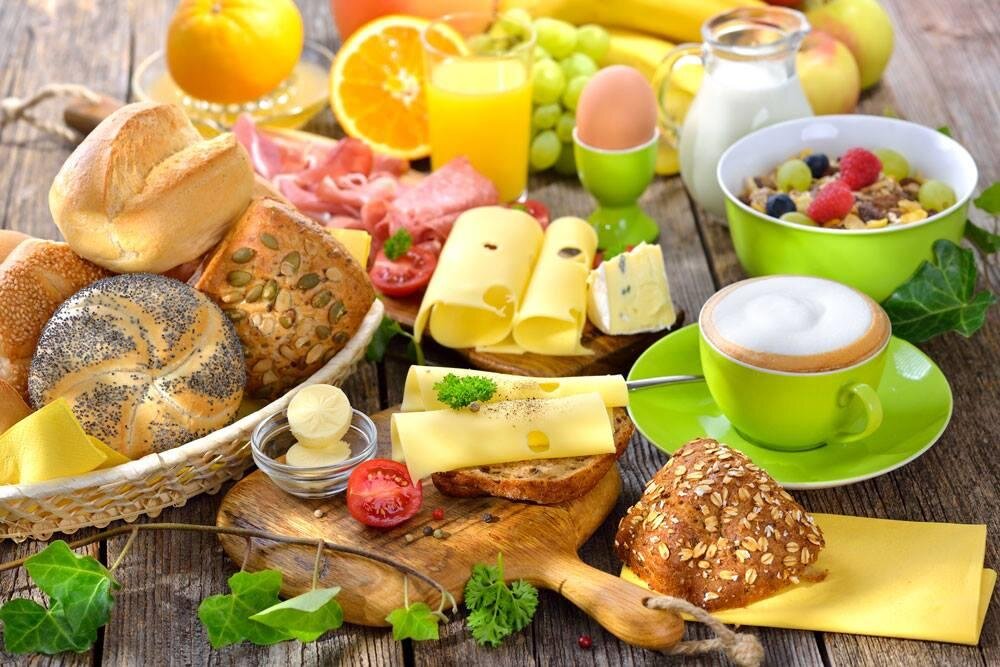 A hearty breakfast with various types of bread, colorful fruit, and drinks. Additionally, there is cheese and yogurt in appetizing bowls.