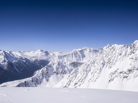 An impressive mountain landscape with snow-covered peaks and clear blue sky. The rugged rocks and deep valleys create a majestic view.