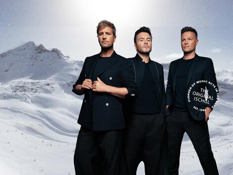 Three men stand in front of a snowy mountain landscape. They are wearing elegant black clothing and looking at the camera.