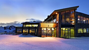 A modern building in the mountains, surrounded by snow. The sunset creates a warm atmosphere.