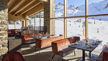 A modern restaurant with large windows that offers a view of a snowy ski slope. The decor is stylish and inviting, perfect for a break after skiing.