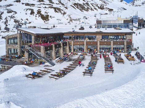 A modern mountain house surrounded by snow-covered mountains. Many loungers are available to enjoy the sun.