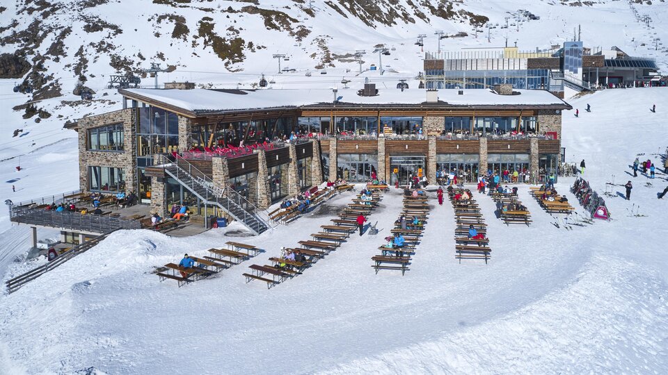 A modern mountain house surrounded by snow-covered mountains. Many loungers are available to enjoy the sun.