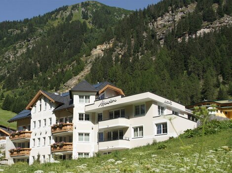 A modern building in the mountains. In the background, green slopes and trees can be seen.