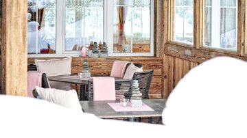 A cozy restaurant with wooden walls and large windows. The tables are elegantly set with pink tablecloths and decorations.