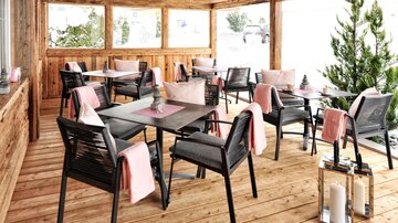 A stylish café with wooden decor and cozy tables. The terrace is furnished with comfortable chairs and soft textiles.