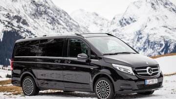 Ein schwarzer Van steht auf schneebedecktem Boden mit Bergen im Hintergrund. Die Landschaft ist winterlich und malerisch.