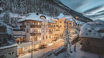 A picturesque winter landscape with snow-covered houses and mountains. The warm lights of the buildings glow in the twilight.