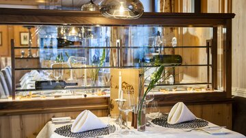 An elegant restaurant with a beautifully laid table. The decor is modern and inviting, with glass and wooden elements.