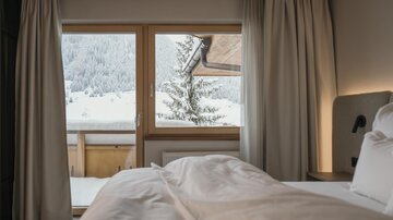A cozy bedroom with a view of a snowy landscape.  
Large windows let in plenty of light and showcase wintery mountains and trees.