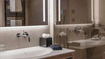 A modern bathroom with a sink and large mirrors. Fresh towels and toiletries are on the shelf.
