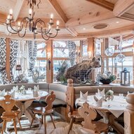 Ein gemütliches Restaurant mit Holzdekor und einer Bärenfigur im Hintergrund. Die Tische sind hübsch gedeckt und schaffen eine einladende Atmosphäre.