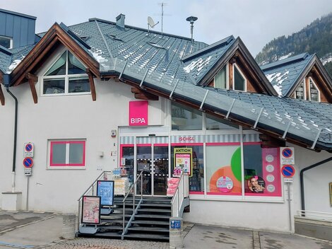 A modern building with a commercial entrance and colorful windows. It is located in a mountainous area and has a sloping roof.