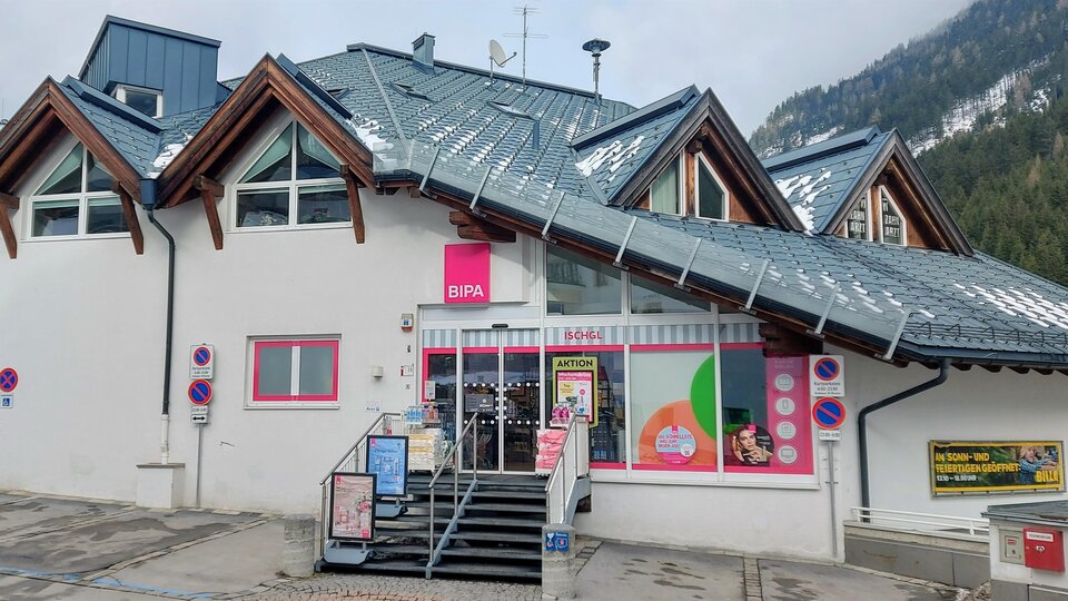A modern building with a commercial entrance and colorful windows. It is located in a mountainous area and has a sloping roof.