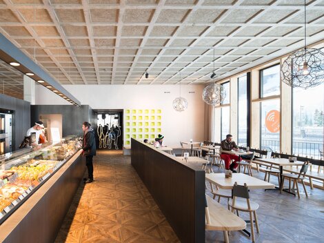 A modern café with large windows, plenty of daylight, and an elegant interior. The counter is decorated with various foods and drinks. | © MPREIS Warenvertriebs GmbH