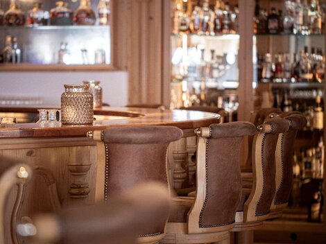 A stylish bar with wooden-clad chairs and elegant glasses. In the background, shelves with various spirits are visible.