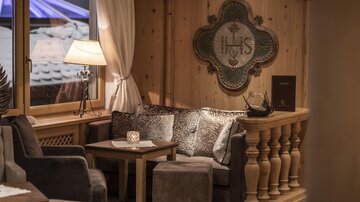 Eine gemütliche Sitzecke mit bequemen Sofa und Stühlen. Sanftes Licht und warme Holzverkleidungen schaffen eine einladende Atmosphäre.