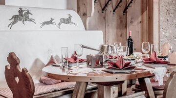 A lovingly set table in a cozy restaurant. Behind the table, a decorative wall painting depicts various riders.