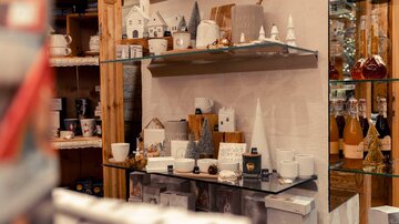 A cozy sales room with several shelves displaying decorative items and gifts. The shelves showcase mugs, small figurines, and bottles.