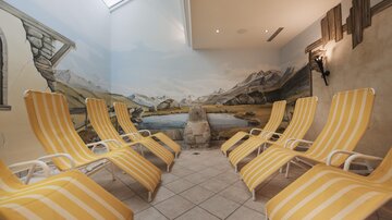 A modern wellness room with yellow striped loungers. The walls are decorated with a picturesque mountain landscape.