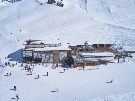 A ski resort with plenty of snow and a large wooden building. Numerous skiers and snowboarders enjoy the wintry landscape.