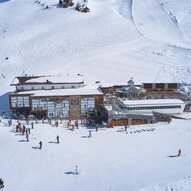 Ein Skigebiet mit viel Schnee und einem großen Holzgebäude. Zahlreiche Skifahrer und Snowboarder genießen die winterliche Landschaft.