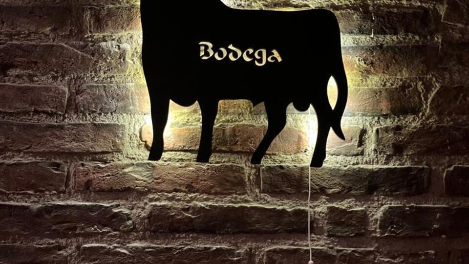 A stylized silhouette of a cow on a brick wall. Below it, "Bodega" is written in curvy script.
