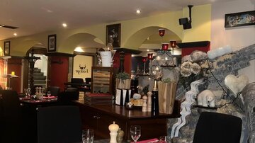A stylish restaurant with dark tables and black chairs. The tables are set with red napkins and glasses, and the walls are tastefully decorated.