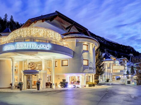An elegant hotel building with beautiful lighting. The surroundings are surrounded by mountains and the sky displays gentle colors of twilight.