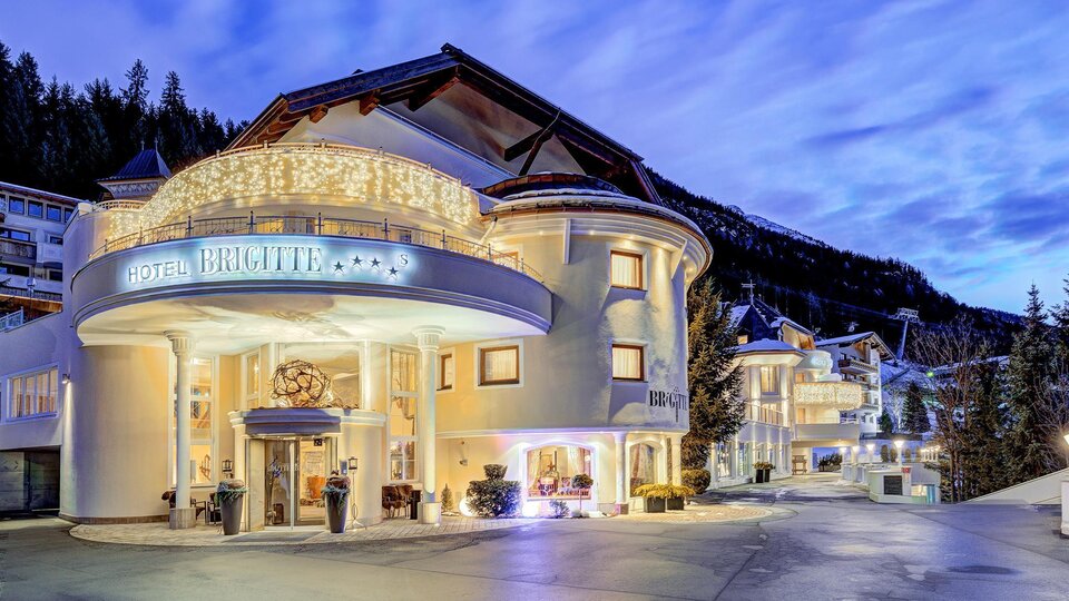 An elegant hotel building with beautiful lighting. The surroundings are surrounded by mountains and the sky displays gentle colors of twilight.