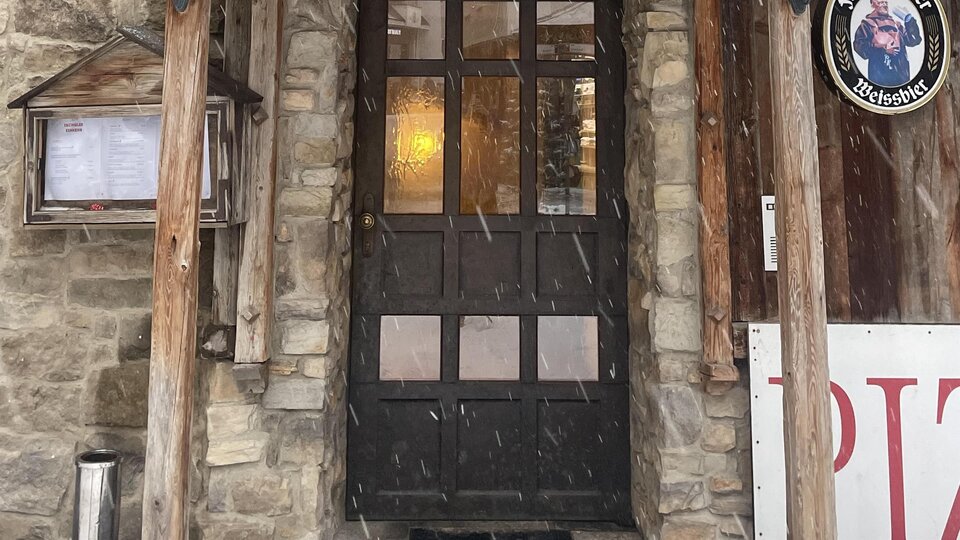 A traditional restaurant with a wooden decorated entrance. Snow covers the roof and creates a cozy atmosphere.