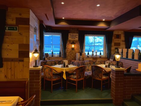 A cozy restaurant with wooden walls and warm lighting. The tables are set for guests and provide an inviting atmosphere.