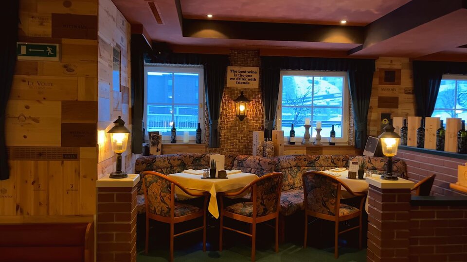 A cozy restaurant with wooden walls and warm lighting. The tables are set for guests and provide an inviting atmosphere.