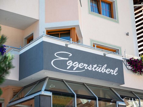 A modern building with a knit front and a large sign reading "Eggerstüberl". Flowers adorn the windows, giving the place an inviting atmosphere.