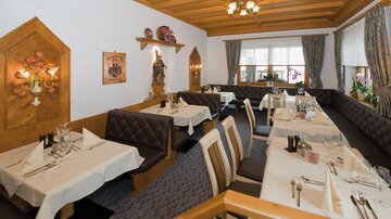 A cozy restaurant with wooden furniture and elegantly set tables. Large windows let in plenty of light and create an inviting atmosphere.