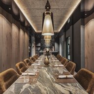 Ein eleganter Restaurantbereich mit einem langen Tisch und gemütlichen Stühlen. Die Atmosphäre ist modern und stilvoll, beleuchtet von großen Lampen.