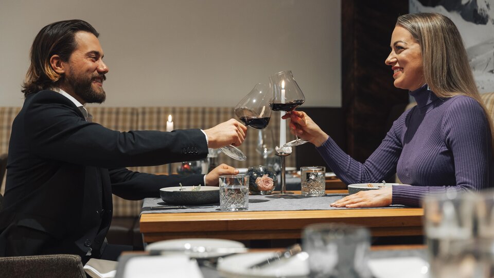 An elegant dinner couple toasts with red wine. The table is set and the atmosphere feels cozy.