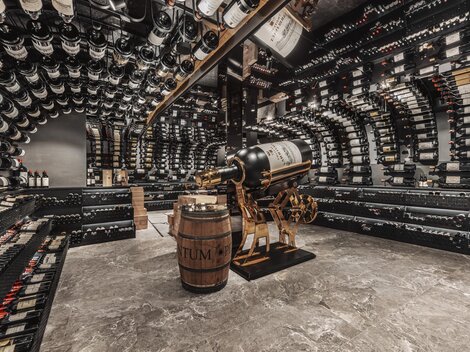 An elegant wine cellar with many shelves full of wine bottles. In the middle stands a barrel and a decorative wine press machine.