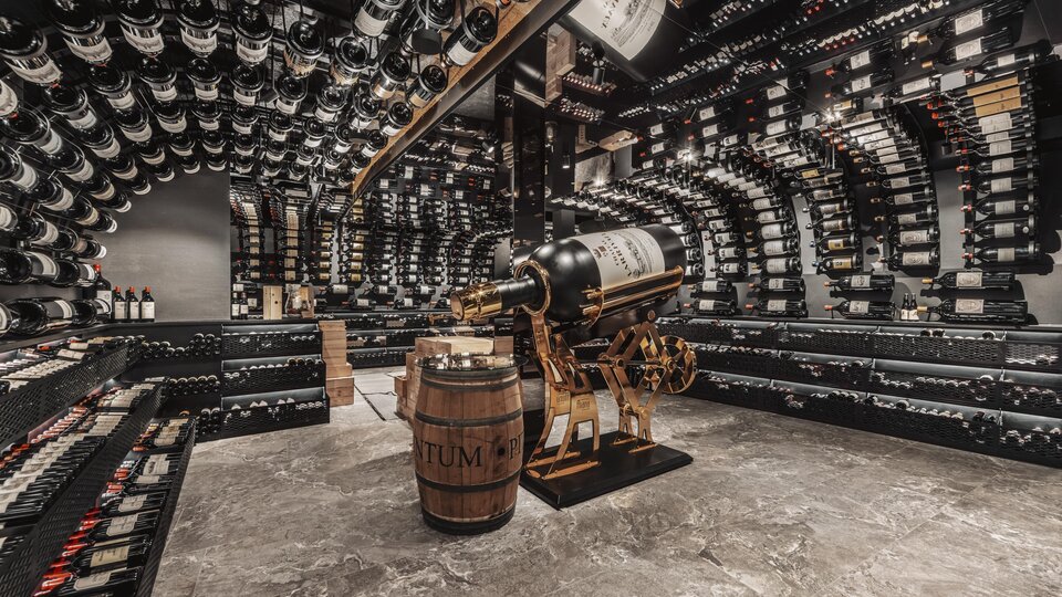 An elegant wine cellar with many shelves full of wine bottles. In the middle stands a barrel and a decorative wine press machine.