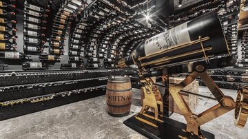 An elegant wine cellar with numerous wine bottles and a large wine barrel. In the foreground, there is an impressive wine bottle on a stylish stand.