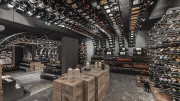 An elegant wine cellar with numerous shelves filled with wine bottles. In the center, wooden boxes are arranged, and candles create a cozy atmosphere.