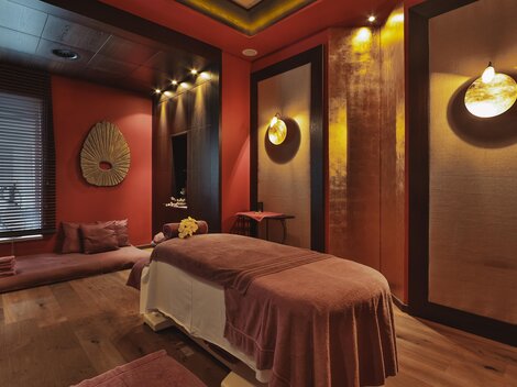 A stylish spa room with a massage table and soft lighting. The walls are painted in warm tones, creating a relaxing atmosphere.